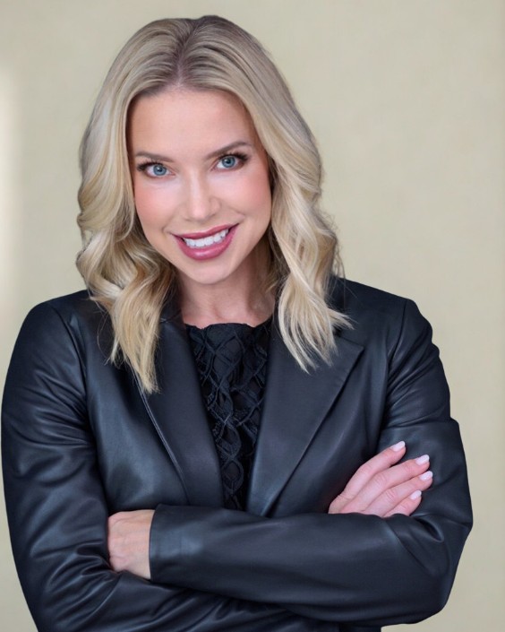 Portrait of Kate Willis in a black leather blazer, arms crossed, smiling